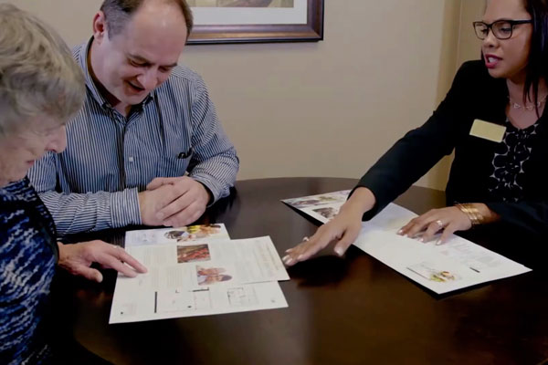 employee sitting at a table with two people explaining information on pieces of paper