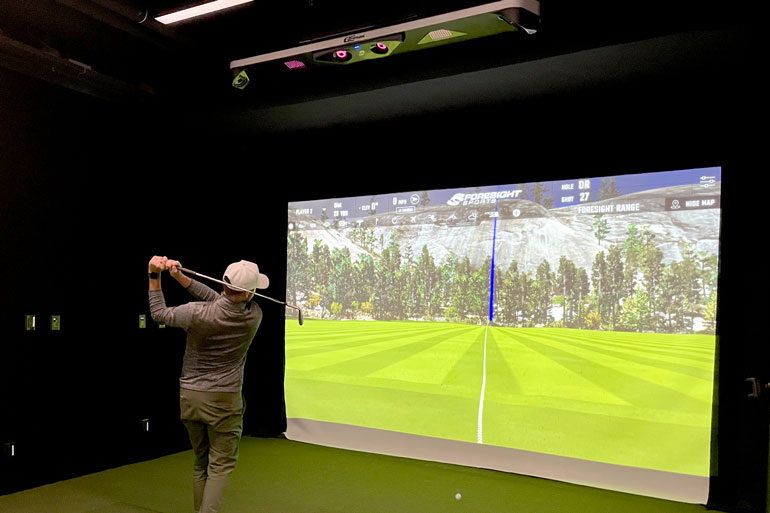 Person swinging club in front of simulator screen