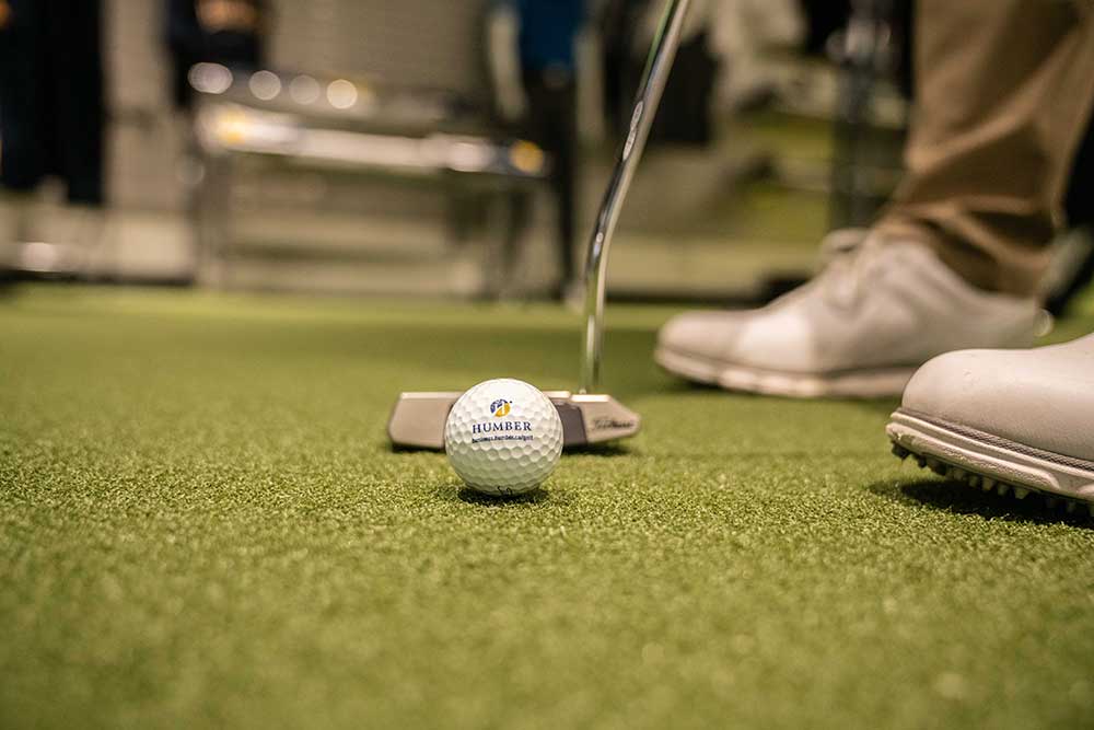 Close up on a man about to putt a Humber branded golf ball