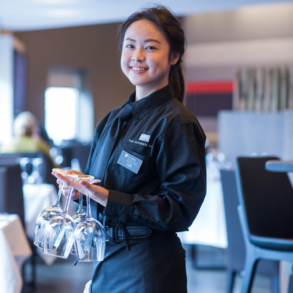 smiling student wearing uniform in the middle of setting table in the Humber Room