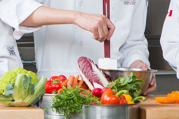 student using a spatula to scrap down bowl with produce in front of them