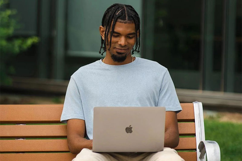 student sitting on a bench using a laptop