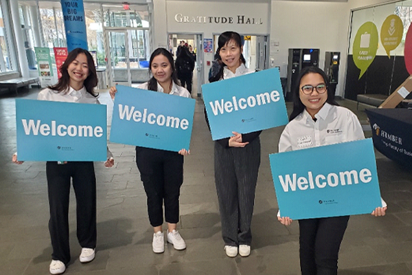 4 people holding Welcome signs outside Gratitude Hall