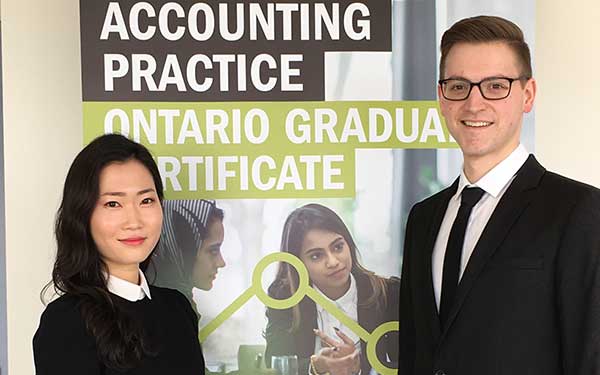 Man and woman in formal attire stand in front of an accounting banner