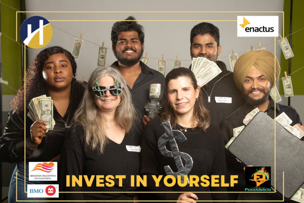 A group of students smiling while holding wads of cash and props for a photo booth picture