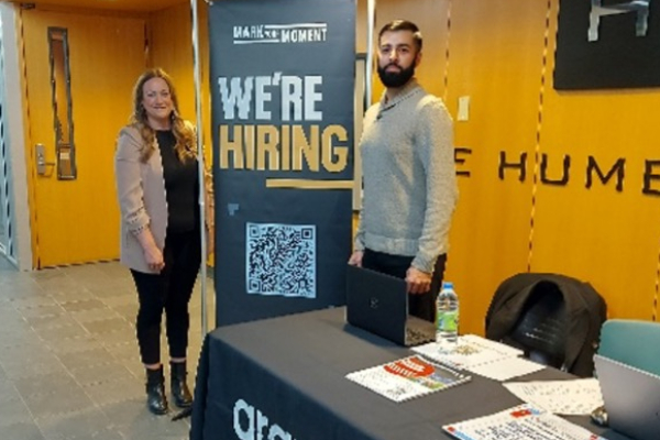 Reps from Aramark standing behind a booth beside a "we're hiring" banner