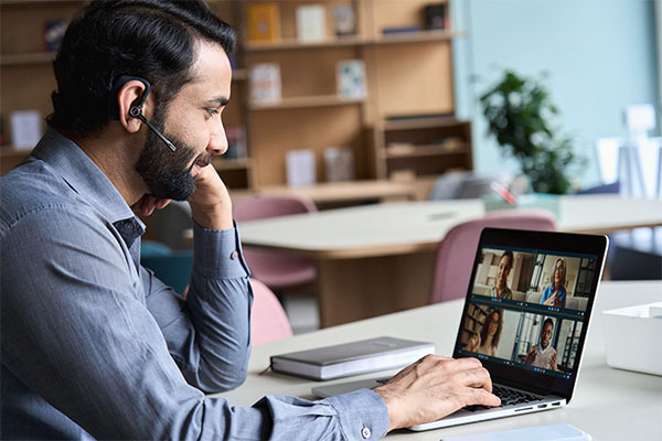 Indian business man wearing headset having virtual team meeting on video conference call, using laptop work from home office talking to diverse people group in remote team zoom online distance chat.