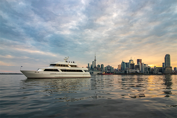 People on an evening sunset party boat cruise leaving Inner Harbour with the Toronto skyline in the background.