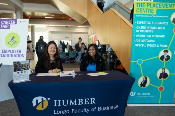 work-integrated learning staff sitting behind a booth and smiling at the career fair