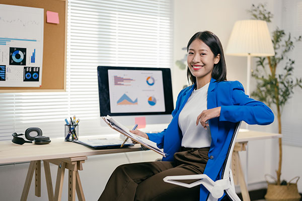 woman in blue blazer sitting in an office setting and using a computer