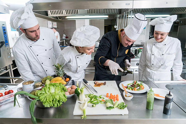 three students watching a head chef cook