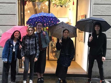 students holding umbrellas posing in front of a retail storefront