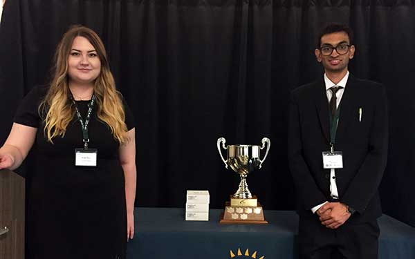 Man and woman on staging with a trophy in between them.