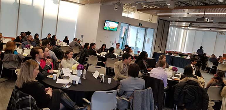 Group of people sitting at tables and listening to a presentation