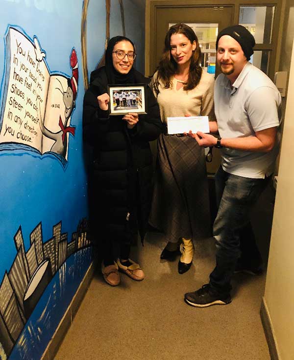Three people standing in a hallway holding up a picture