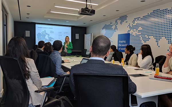Students sitting around a conference table listening to a woman speak