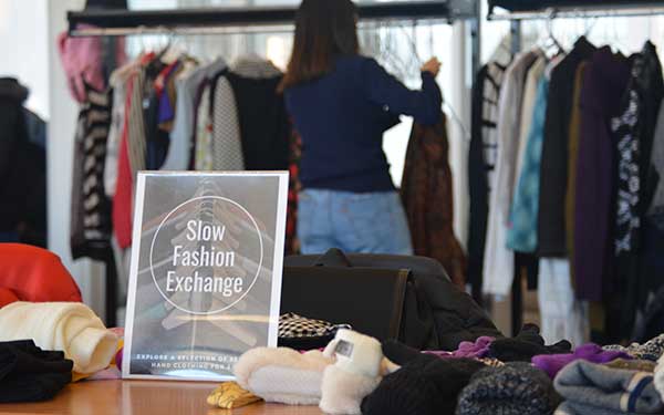 table with sign and cloth ontop with a woman going through a rack of clothes in the background